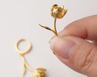 May include: A pair of gold-toned earrings featuring a delicate tulip design. The earrings are made of metal and have a hoop-style closure.