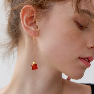 May include: A pair of gold dangle earrings with a red square-shaped gemstone pendant.