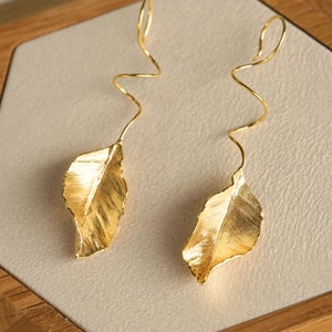 May include: A pair of gold leaf earrings with a twisted wire design. The leaves are textured and have a slightly irregular shape.
