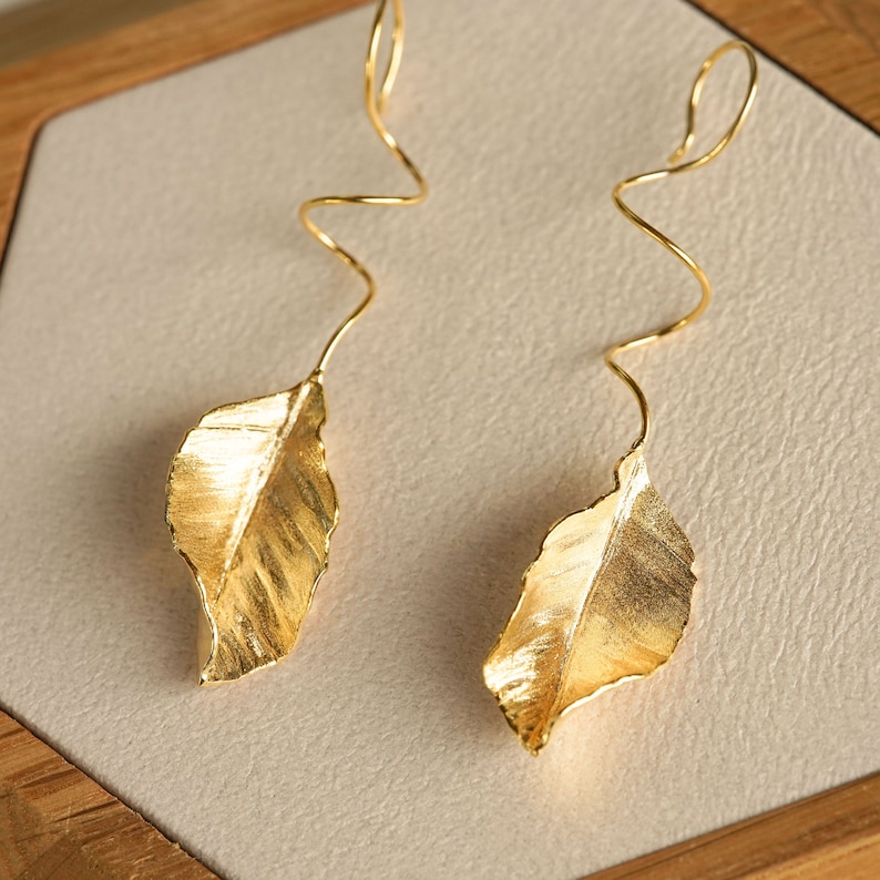 May include: A pair of gold leaf earrings with a twisted wire design. The leaves are textured and have a slightly irregular shape.
