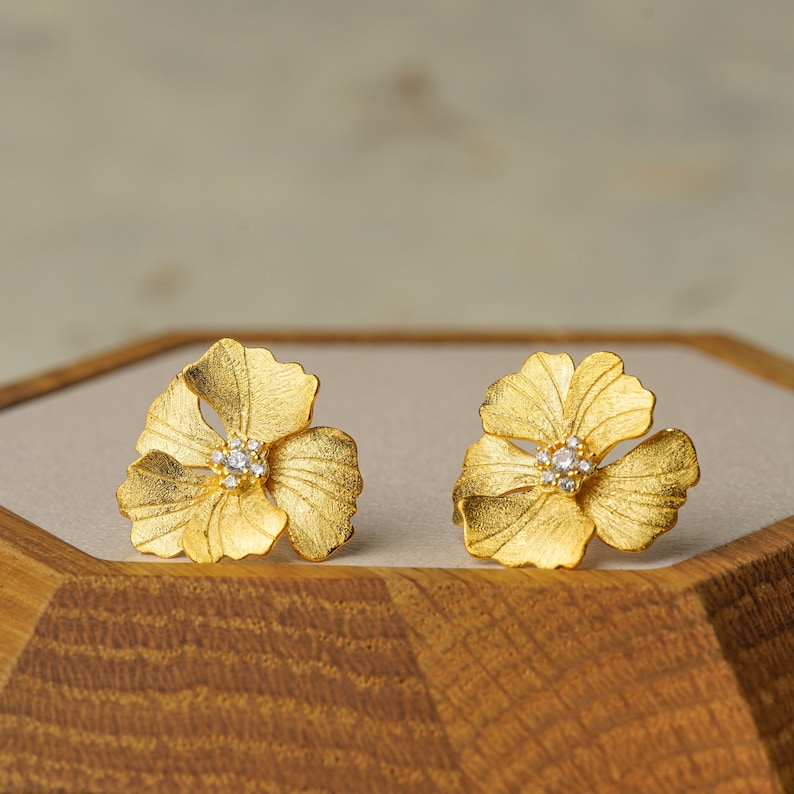 May include: A pair of gold flower-shaped earrings with a single clear diamond in the center of each flower.