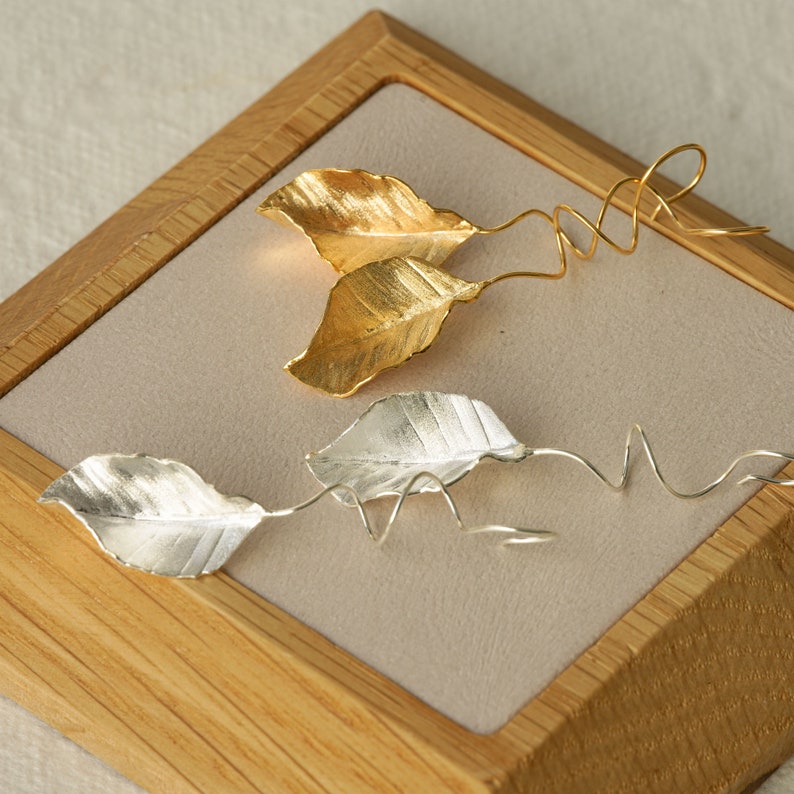 May include: A pair of leaf-shaped earrings with a twisted wire design. One pair is gold and the other is silver.