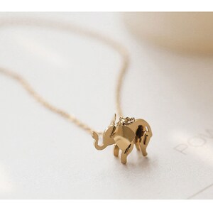 May include: A gold-colored elephant pendant necklace. The elephant charm is detailed with visible legs, trunk, and ears. The necklace chain is delicate and gold-toned, creating a simple and elegant jewelry piece.
