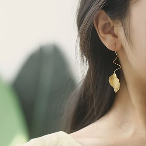 May include: Gold leaf earrings with a twisted wire design. The earrings are dangling and feature a leaf shape.
