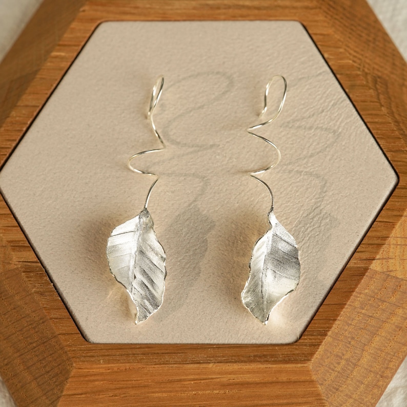 May include: A pair of silver earrings with a leaf design. The earrings are made of twisted wire and have a delicate, organic look.