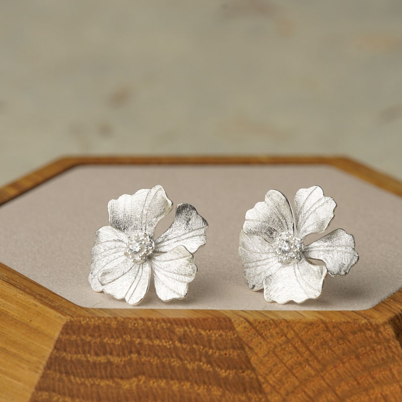 May include: A pair of silver flower-shaped earrings with a small clear stone in the center of each flower.