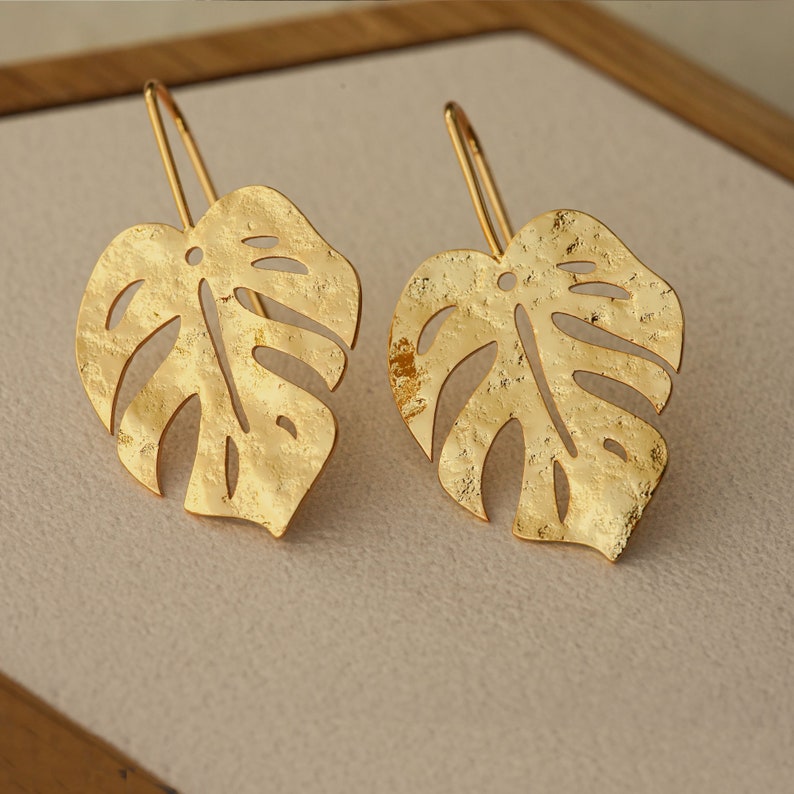 Two gold monstera leaf earrings with a textured finish.