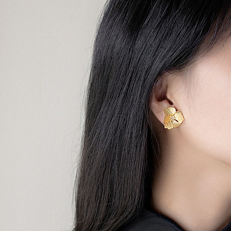 May include: Gold flower-shaped earrings. The earrings are a delicate design with a textured surface.