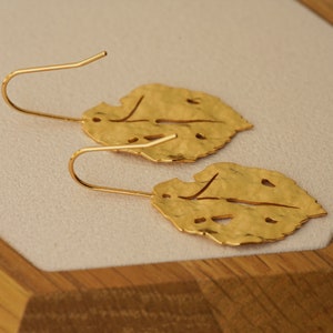 May include: A pair of gold leaf-shaped earrings with a hammered texture and cut-out details. The earrings have a simple hook closure.