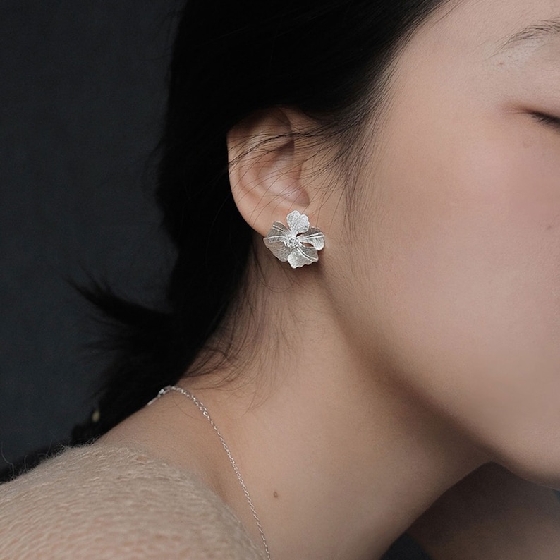 May include: Silver flower stud earrings. The earrings are small and delicate, with a detailed floral design.