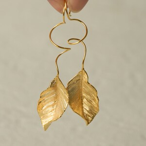 May include: Gold leaf earrings with a twisted wire design. The leaves are textured and have a slightly hammered finish.