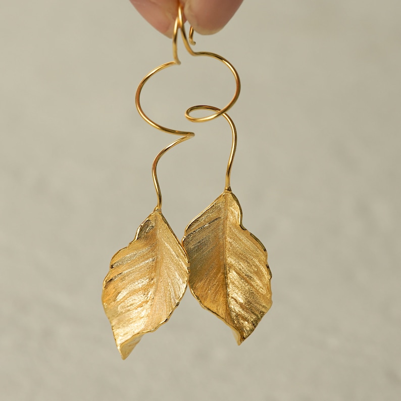 May include: Gold leaf earrings with a twisted wire design. The leaves are textured and have a slightly hammered finish.