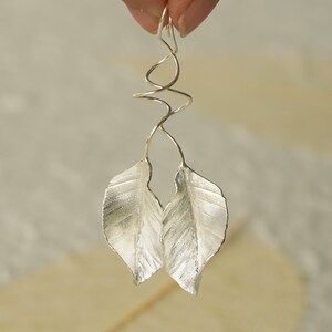 May include: Silver earrings with a twisted wire design and two leaf-shaped pendants.