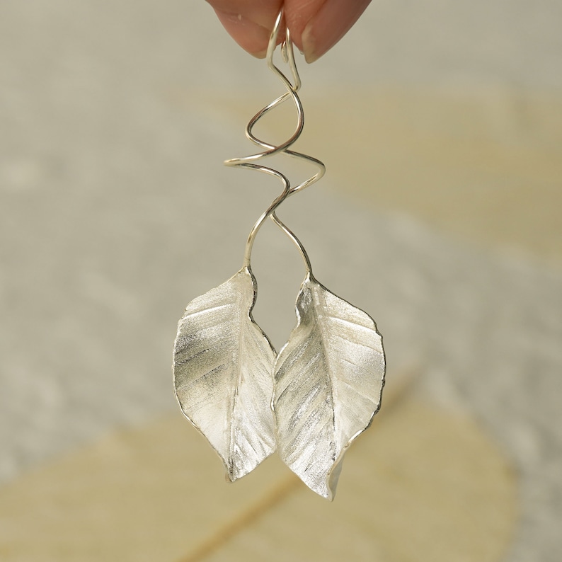 May include: Silver earrings with a twisted wire design and two leaf-shaped pendants.