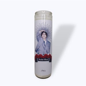 May include: A white candle with a printed image of a man in a gray suit with a black tie. The man is holding his hand to his head. The candle has a red rose design at the bottom and the words "Saint Han" printed on a black banner.