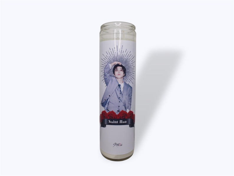 May include: A white candle with a printed image of a man in a gray suit with a black tie. The man is holding his hand to his head. The candle has a red rose design at the bottom and the words "Saint Han" printed on a black banner.