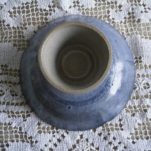 May include: A small, blue and white ceramic dish with a shallow, round well in the center. The dish has a glazed finish and a slightly uneven rim.
