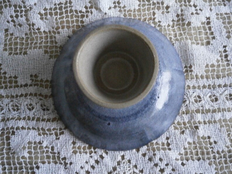 May include: A small, blue and white ceramic dish with a shallow, round well in the center. The dish has a glazed finish and a slightly uneven rim.