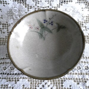 May include: A small, white ceramic bowl with a brown rim. The bowl has a floral design with blue and pink flowers.