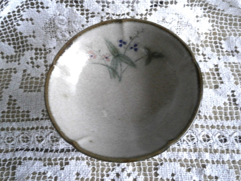 May include: A small, white ceramic bowl with a brown rim. The bowl has a floral design with blue and pink flowers.
