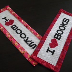 May include: Two handmade bookmarks with pink fabric borders. One bookmark says "I love books" with a red heart and the other says "I love books" with a red heart.