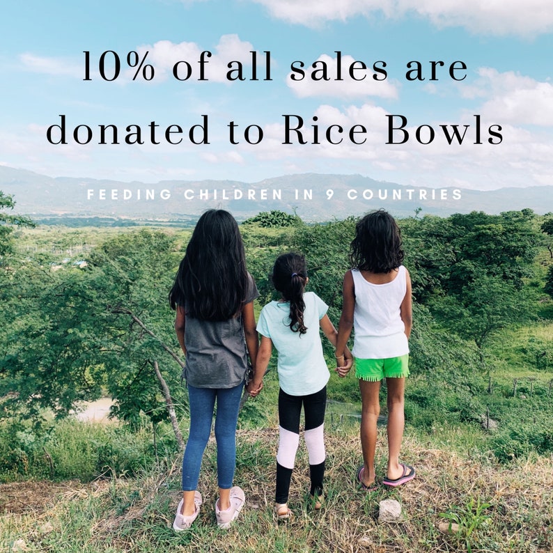 May include: Three girls stand on a grassy hilltop, looking out at a lush green landscape. The text "10% of all sales are donated to Rice Bowls FEEDING CHILDREN IN 9 COUNTRIES" is displayed at the top of the image.