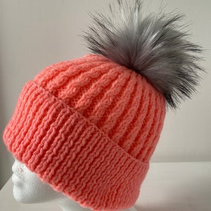 May include: A pink knitted beanie with a black and white faux fur pom pom.