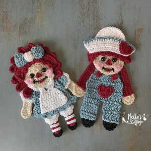 May include: Two crocheted rag dolls, one with a red and white dress and the other with blue overalls. Both dolls have red yarn hair and a heart-shaped design on their chest.