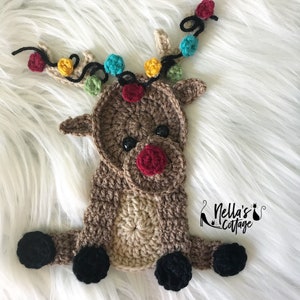 May include: A crocheted reindeer ornament with a brown body, black hooves, and a red nose. The reindeer has a string of colorful lights wrapped around its antlers.