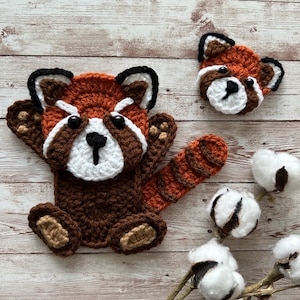 May include: Two crocheted red panda plushies. The larger plushie is brown with an orange tail and white face. The smaller plushie is red with a white face. Both plushies have black eyes and noses.