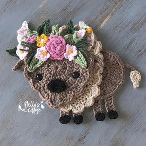 May include: A crocheted brown and beige animal with a flower crown. The crown is made of pink, white, and yellow flowers. The animal has a brown nose and black eyes.