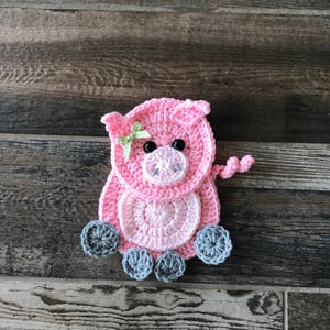 Op de afbeelding: Een roze gehaakt varken met een groene strik, grijze gehaakte pootjes en zwarte ogen.