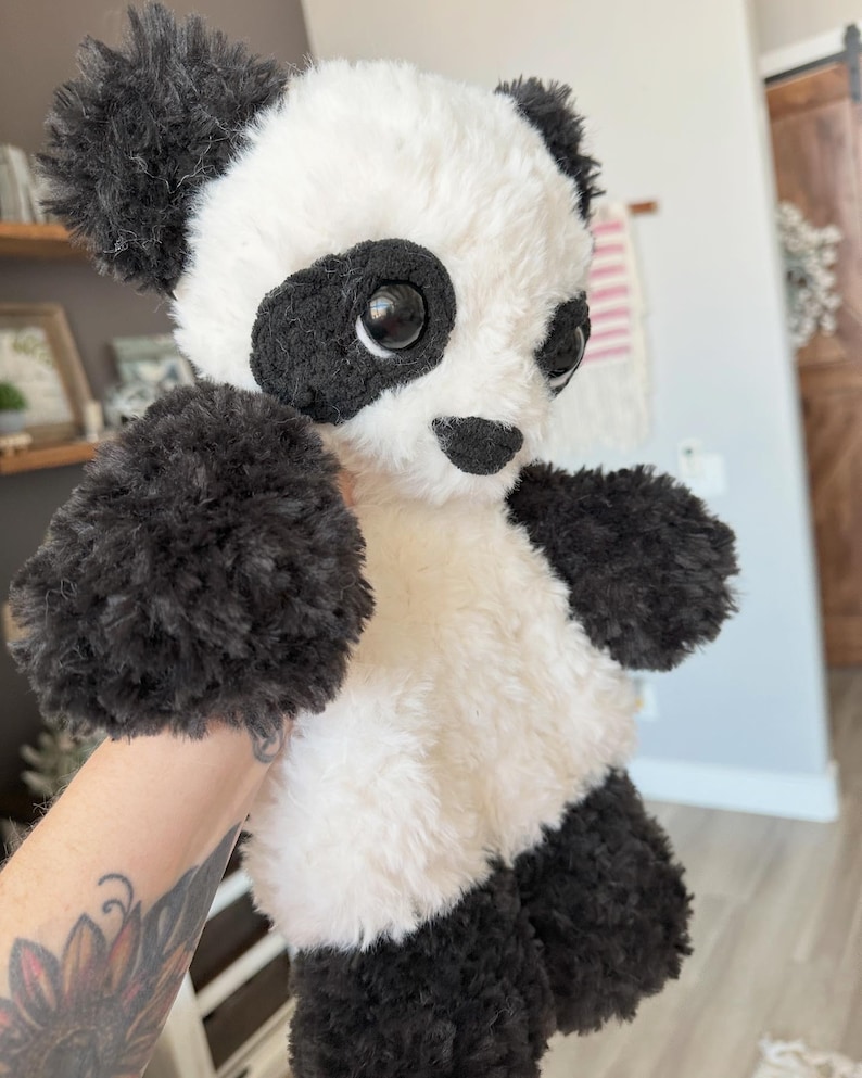 May include: A plush panda bear with black and white fur. The panda has black fur around its eyes, ears, arms, and legs. The bear's body is white, and it has large, black eyes and a small black nose. The panda is a stuffed animal.