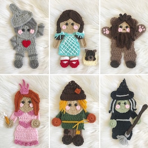 Puede incluir: Una colección de seis apliques de personajes de ganchillo de El Mago de Oz. Los personajes incluyen el Hombre de Hojalata, Dorothy, el León Cobarde, una princesa, el Espantapájaros y la Bruja Malvada. Cada aplique está hecho a mano con hilo y presenta rasgos faciales detallados.