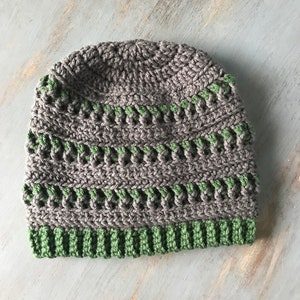 May include: A gray and green crocheted beanie hat. The hat has a ribbed brim and a textured pattern.