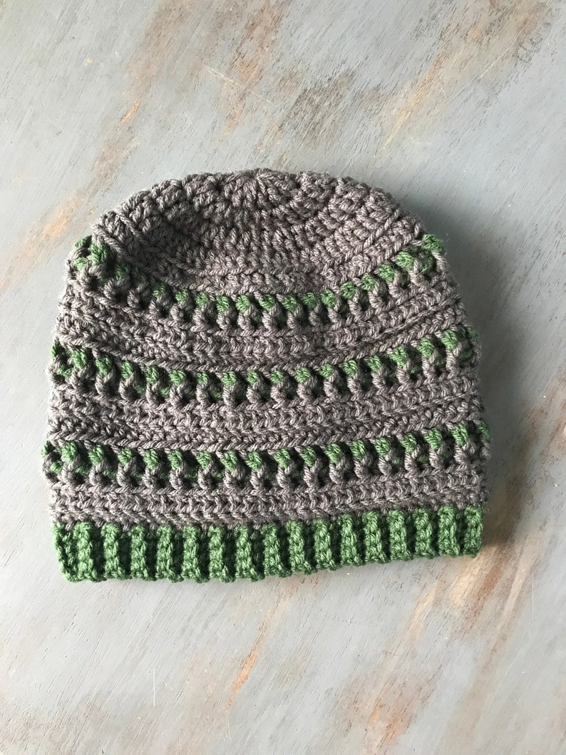 May include: A gray and green crocheted beanie hat. The hat has a ribbed brim and a textured pattern.