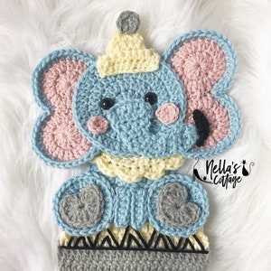 May include: A crocheted blue elephant with pink ears, a yellow hat, and gray feet. The elephant is standing on a gray and black striped base. The text "Nella's Cottage" is visible in the lower right corner of the image.