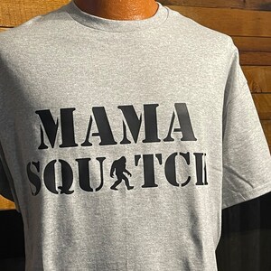 May include: Gray t-shirt with black text that reads "Mama Squatch" with a silhouette of Bigfoot walking.