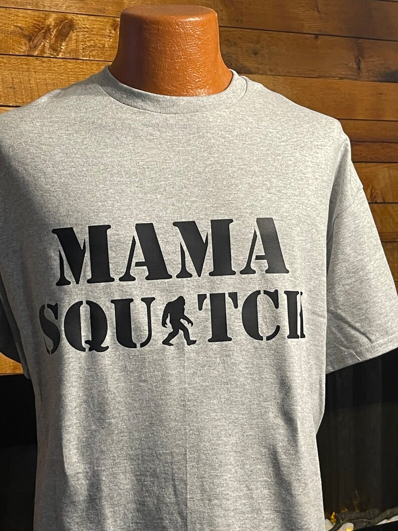 May include: Gray t-shirt with black text that reads "Mama Squatch" with a silhouette of Bigfoot walking.
