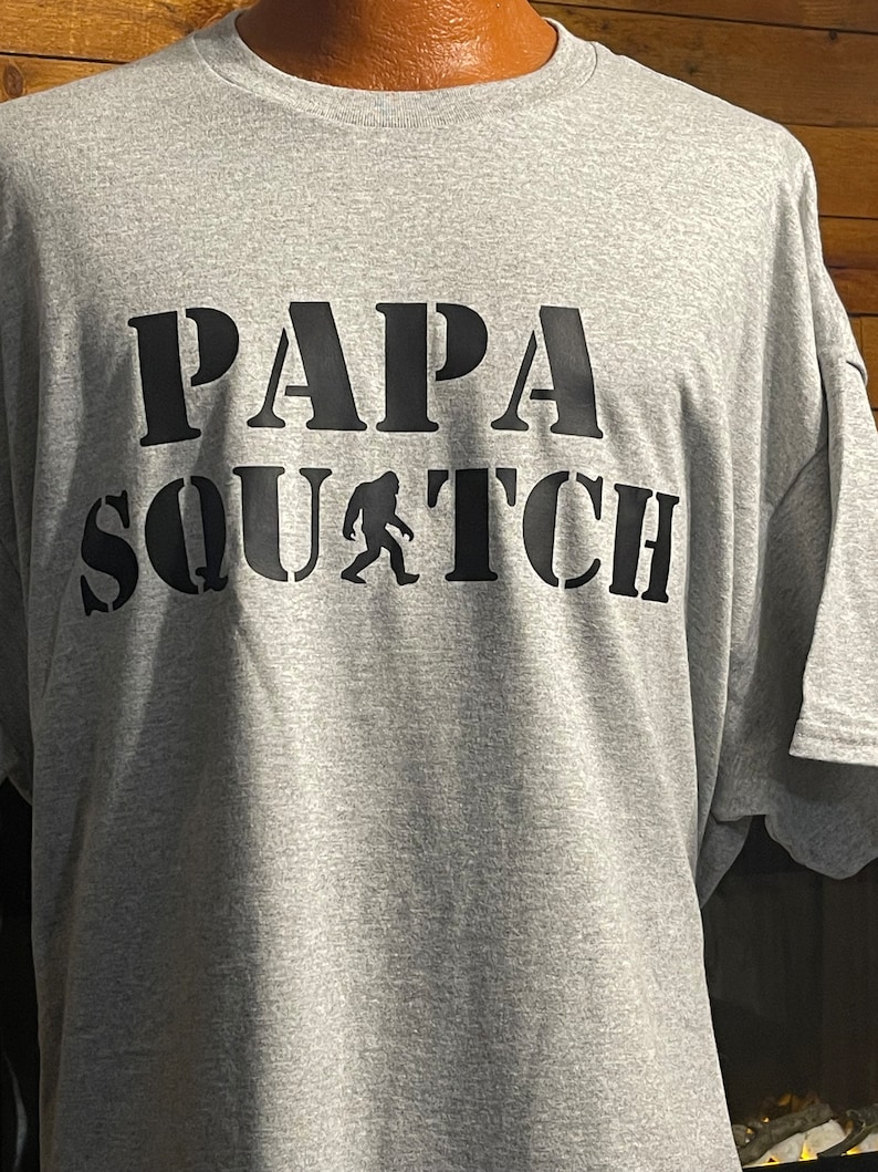 May include: Gray t-shirt with black text that reads "Papa Squatch" with a silhouette of Bigfoot in between the words.