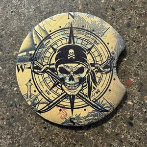 May include: A round, beige coaster with a compass design featuring a skull wearing a pirate hat. The compass points are labeled with the directions N, NE, E, SE, S, SW, W, and NW. The skull is surrounded by crossed swords.