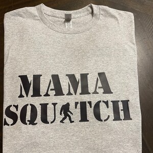 May include: Gray t-shirt with black text that reads "Mama Squatch" with a silhouette of Bigfoot.