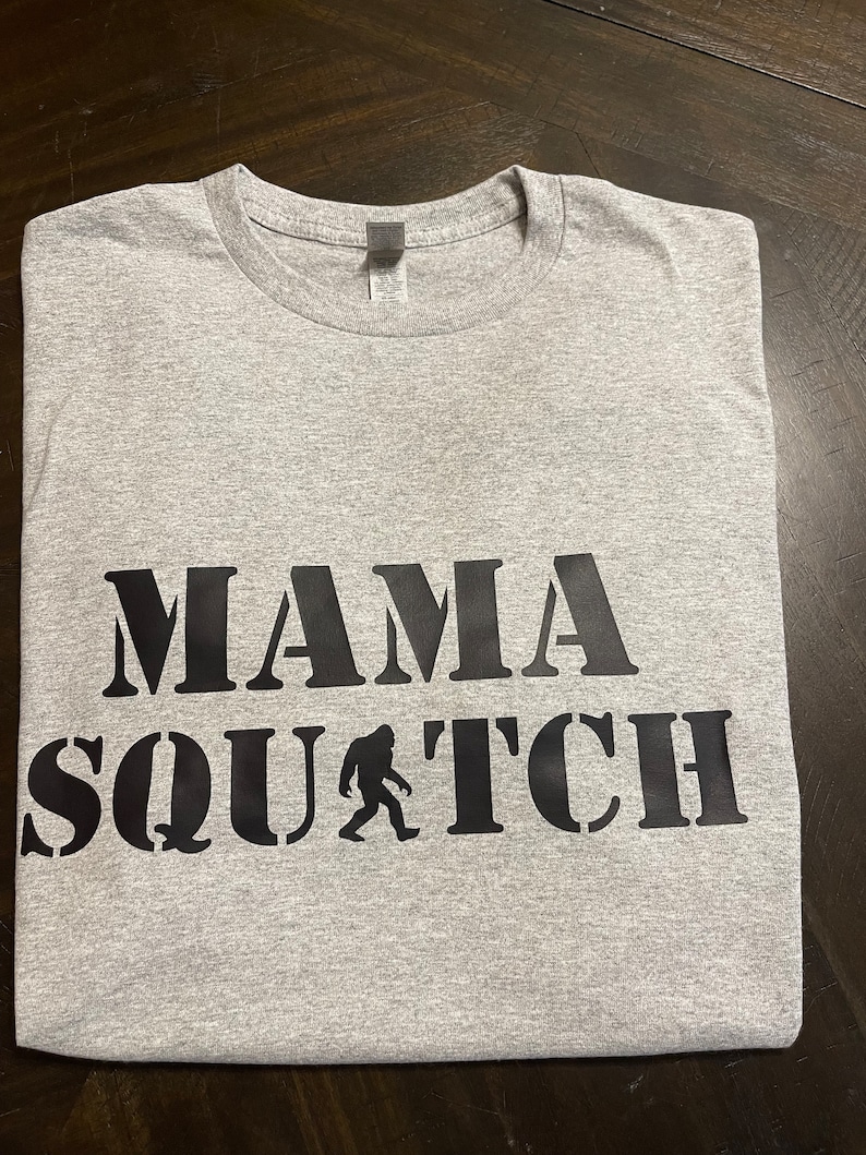 May include: Gray t-shirt with black text that reads "Mama Squatch" with a silhouette of Bigfoot.