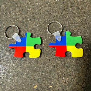 May include: Two colorful puzzle piece keychains with a red, yellow, blue, and green design. Each keychain has a silver ring and a clear plastic loop.