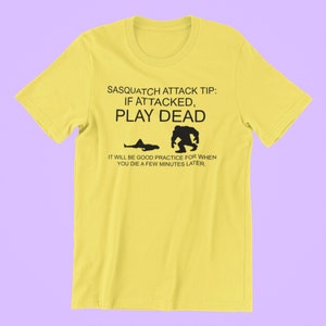 May include: Yellow t-shirt with a black graphic that says "Sasquatch Attack Tip: If Attacked, Play Dead. It will be good practice for when you die a few minutes later."