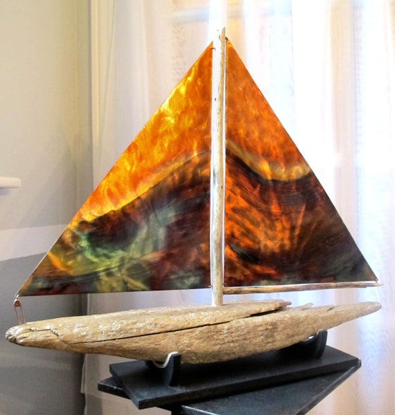 This sailboat sculpture is composed of flame painting copper sails and a driftwood hull. The support is in wood.