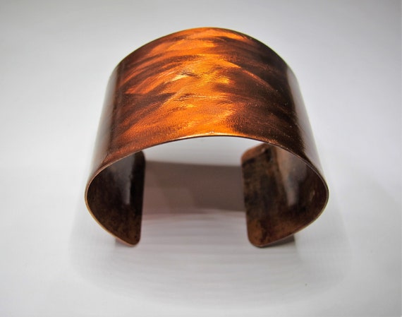 Copper Bracelet that was textured and flame painted . The cuff is covered by a protective coat
