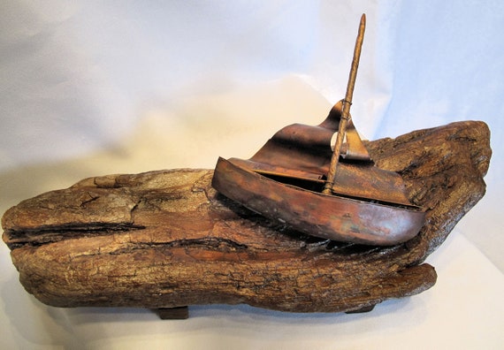 This sailboat sculpture is composed of flame painting copper sails and a driftwood hull. The support is in wood.