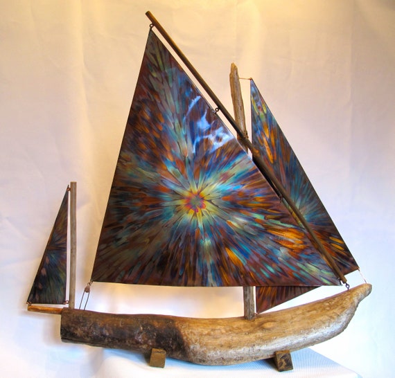 This sailboat sculpture is composed of flame painting copper sails and a driftwood hull. The support is in wood.