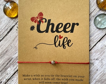 May include: Red string bracelet with a silver star charm and a card that says "#Cheer life" and "Make a wish as you tie the bracelet on your wrist, when it falls off, the wish you made will soon come true!"